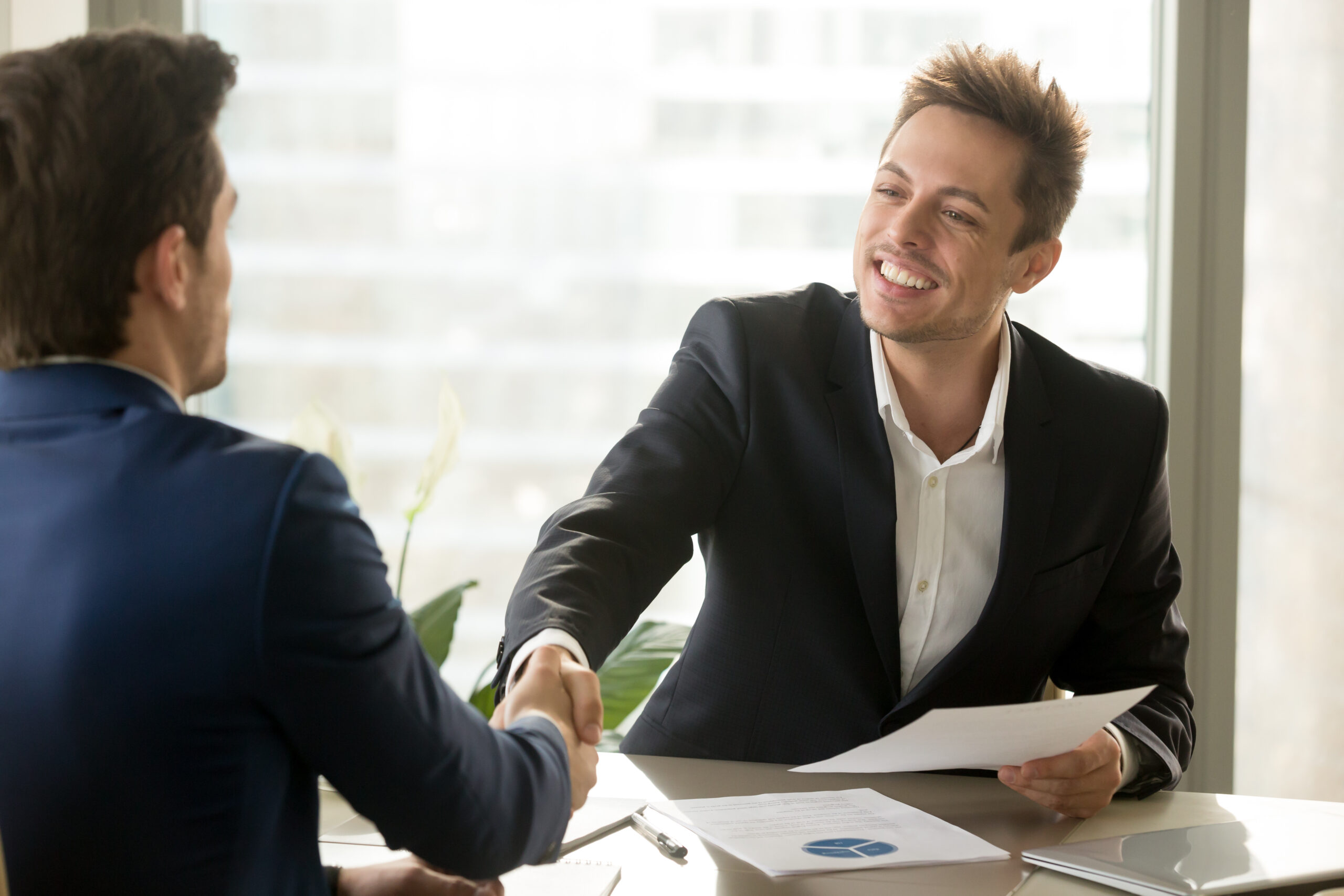 Smiling manager and client handshaking, satisfied businessmen shaking hands offering financial contract, support, help, good business deal, reaching agreement, business analytics, graphs stats on desk